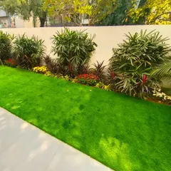 A vibrant front yard with a perfectly manicured artificial turf lawn bordered by a mix of green shrubs and colorful flowers for a clean, evergreen look.