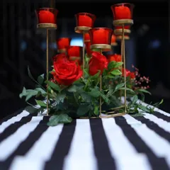 A chic and modern centerpiece for a 40th birthday party. Red roses and candles in red glass holders are arranged on a black and white striped table runner, creating a bold and sophisticated look.