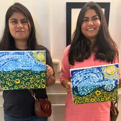 Two happy participants holding up their unique interpretations of a 'Starry Night' inspired sunflower field. It's amazing to see how each person's style shines through.