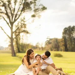 A family shares a tender moment during a picnic, with the parents focused lovingly on their baby. The golden hour lighting and natural park setting create a warm and intimate atmosphere.