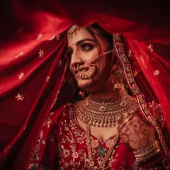 A stunning close-up of a bride, framed by her red dupatta. The lighting beautifully highlights her features, jewelry, and the intricate details of her nath.