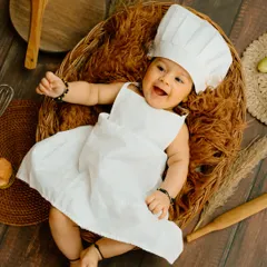 A belly laugh from our little chef! The rustic wooden props and chef's outfit create an authentic and adorable kitchen scene.