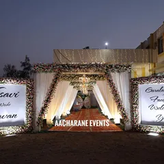 A beautiful and welcoming entrance for a reception. The walkway is defined by white drapes and warm lighting, leading to the main hall, with floral signboards on either side welcoming the families.