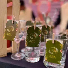 Custom floral-themed tags with the couple's monogram and wedding hashtag, '#IAMINLOVE', clipped to each glass.