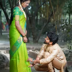 A sweet and traditional pre-wedding moment, where the groom-to-be helps his fiancée with her footwear. This candid-style shot captures a gesture of care and affection between the couple.