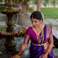 A moment of quiet reflection for the bride. Her vibrant purple and pink saree and traditional gold jewelry are beautifully highlighted in this classic portrait.