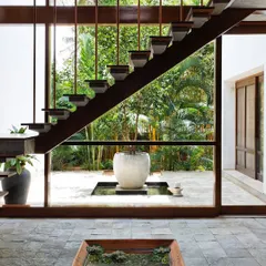 A floating staircase becomes a sculptural element against a wall of glass, dissolving the boundary between the home and the lush tropical garden outside. This design for 'The Tropical House' is a direct expression of our passion for creating homes that live and breathe with nature.