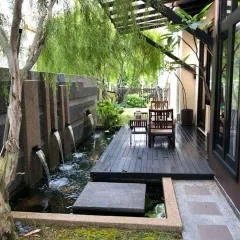 A modern water feature with multiple spouts creating gentle streams into a pond. This design, set against a textured stone wall and surrounded by lush greenery, adds a sophisticated and calming element to the landscape.