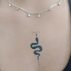 A close-up of the minimalist snake tattoo. The simple black lines and dot work create a very sleek and modern design.
