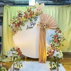 A stylish engagement backdrop with a large white circular panel and earthy-toned floral arrangements. A touch of gold fabric adds a bit of shimmer, and the couple's names can be added for a personalized touch.