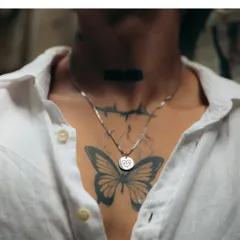 A silver-toned round pendant engraved with a simple, hand-drawn style heart. This piece, worn against a butterfly tattoo, shows how my jewelry can complement your personal story and style.