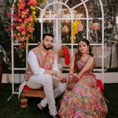 Arya and her groom seated before their ceremony, framed by a beautiful floral arch. This shot captures the calm before the celebration begins, highlighting the stunning decor and traditional attire.