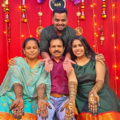 A heartwarming family photo showcasing the bride's portrait mehendi. She is pictured with her parents and brother, with her parents' faces beautifully drawn on her hands.
