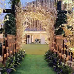 This enchanting entranceway uses an arch of rustic branches and white blossoms, lined with candles. The path leads into a lush green lawn, creating a beautiful transition from the entrance to the main event area.
