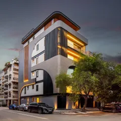 This builder floor in Patel Nagar, Delhi, demonstrates how modern geometry can redefine an urban streetscape. The facade's composition of symmetrical curves, aluminum louvers, and textured mortar creates a balanced and restrained look, especially when highlighted by evening lights.