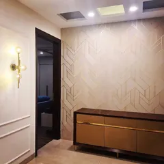 We elevate living spaces with sophisticated wall treatments. This design features elegant geometric-patterned wallpaper paired with classic wall moulding and a modern brass sconce, adding depth and character to the entryway.