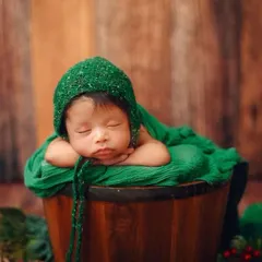 This classic 'potato sack' pose is a favorite for showing how curled up and tiny newborns are. The rich green wrap and rustic wooden backdrop create a beautiful, earthy portrait.