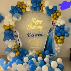 A magical Frozen-themed birthday party. This setup features a circular balloon arch in icy blue, white, and gold, with cutouts of Elsa and Olaf, all centered around a 'Happy Birthday' neon sign for a cool celebration.