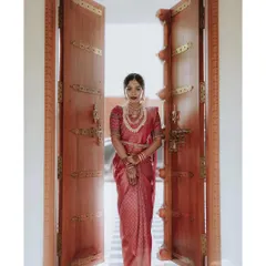 A grand bridal entrance. This stunning portrait of the bride in a red silk saree, framed by magnificent traditional doors, creates a powerful and regal image.