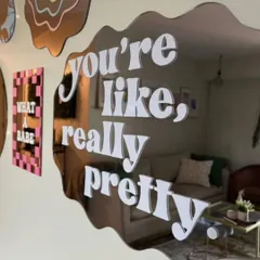 Add a personal touch to your room with a custom quote mirror. This piece features a trendy wavy shape and the phrase 'you're like, really pretty' in a bold font, turning a daily affirmation into decor. We can create any shape and apply any text or design you envision.