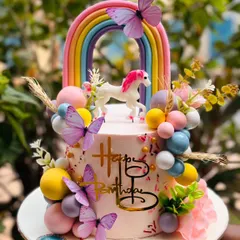 A dreamy unicorn and rainbow cake for Kaira's birthday. This design is adorned with pastel-colored spheres, delicate butterflies, and a beautiful rainbow, creating a truly magical centerpiece.