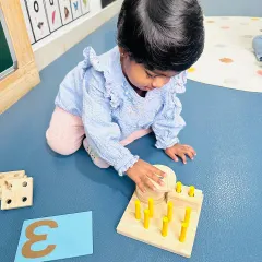 This child is fully engaged in a counting activity, matching pegs to holes. This is a perfect example of a hands-on task that develops fine motor skills alongside early math understanding.