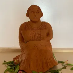 A terracotta sculpture of a woman, seated in quiet contemplation. The detailed texture of her dress and the gentle expression on her face tell a story of inner peace.