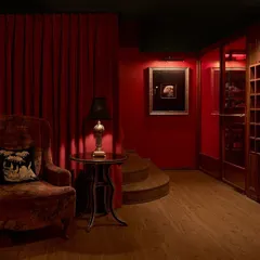 The foyer of the ZLB23 speakeasy, where deep red walls and a plush velvet armchair create an atmosphere of vintage luxury. The design guides guests through a series of unfolding spaces, building anticipation.
