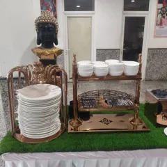 Organization is key in a buffet line. This station features neatly stacked plates, bowls, and cutlery in stylish copper-toned stands, ensuring easy access for guests.