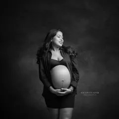A joyful and candid black and white portrait. The mother-to-be's natural smile and the soft lighting create a warm and authentic moment.