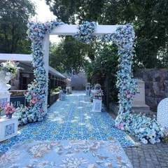 A beautiful entrance for a daytime event, featuring a carpet of blue patterned tiles leading to a floral arch of blue and white hydrangeas, setting a fresh and serene tone.
