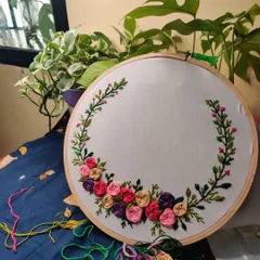 The beginning of a floral wreath embroidery project. This shows the initial flowers stitched, with the threads ready for the next part of the design.