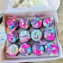 A closer look at the mermaid-themed cupcakes, featuring a mix of designs. Some have colorful frosting swirls with mermaid tail toppers, while others are personalized with the birthday girl's name and age.