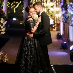 A romantic portrait of the couple at their reception. Dressed in a stunning black gown and tuxedo, they share an intimate embrace against a backdrop of beautiful bokeh lights.