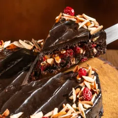 Here’s a close look at our star creation. You can see the rich, dense texture of the oat flour sponge, the bright pop of our house-made cranberry compote, and the generous topping of toasted almonds. The glossy finish comes from a silky vegan chocolate ganache we make with coconut milk.