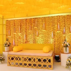 For this indoor haldi ceremony, I created a complete yellow theme. The backdrop is made of woven genda phool, with hanging floral tassels, and the seating is a simple wooden bench, creating a clean and modern look.