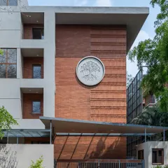 The facade of this Bengaluru apartment building showcases our approach to modern Indian architecture. The intricate exposed brickwork and custom tree-of-life emblem are a testament to our focus on craftsmanship and creating buildings with a unique identity.