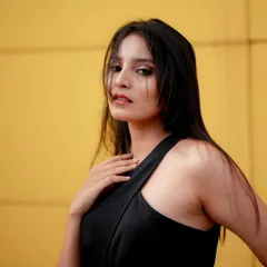 A striking portrait using a bold yellow wall as a backdrop. The simple background makes the model's expression and the clean lines of her black top the main focus of the image.