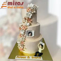 A cake that tells a love story. This elegant, three-tiered engagement cake captures a beautiful proposal moment, complete with a custom figurine, a photo of the happy couple, and a cascade of delicate, handmade sugar flowers.