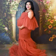 A classic studio portrait with a beautiful floral arch backdrop. The mom-to-be looks stunning in a rust-colored mermaid gown with dramatic tulle sleeves.