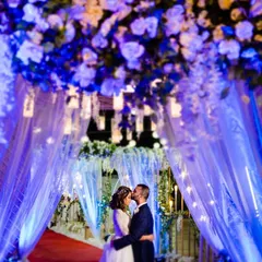 A 'tunnel of love' created by dramatic blue lighting and flowing drapes. This wide shot turns a wedding venue entrance into a magical, romantic portrait location.