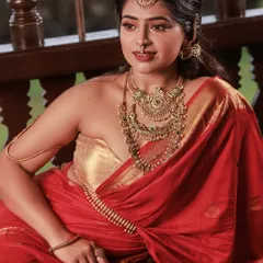 A classic South Indian bridal look captured with an editorial eye. The rich red saree, layered temple jewelry, and the relaxed yet elegant pose come together to create a picture of timeless grace.