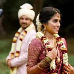 A candid shot of the bride with a beautiful smile, while the groom stands in the soft-focused background. This composition highlights the bride's joy on her wedding day.