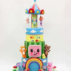 The full view of the four-tier Cocomelon cake, complete with a rainbow, carousel, and all the favorite characters like JJ, TomTom, and YoYo.