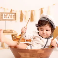 The little chef is ready to cook up some fun! Dressed in a chef's uniform, this baby sits in a giant mixing bowl, creating a playful and adorable scene.