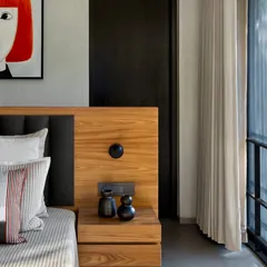 A detail of a bedroom in the Mango Orchard House. The custom wooden headboard integrates a bedside table and electricals, showcasing our focus on smart, built-in solutions. The vibrant artwork adds a pop of color to the otherwise neutral room.