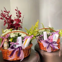 Classic wicker basket hampers filled with goodies and fresh flowers. The purple ribbon and floral arrangements add a touch of sophistication to these celebration gifts.