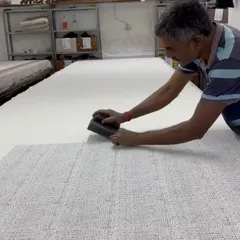 The steady hand of a master artisan at work. Here, one of our printers carefully aligns a teak block to create a seamless pattern on a long stretch of fabric, a skill honed over decades of practice.