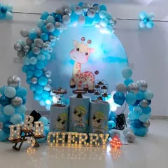 A cute and gentle animal theme featuring a friendly giraffe. This setup for Cherry's 2nd birthday uses a blue and silver color palette, a circular backdrop, and light-up marquee letters for the name.