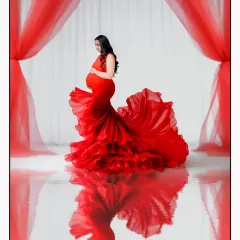 A stunning solo portrait featuring a vibrant red maternity gown with a long, ruffled trail, creating a beautiful reflection on the studio floor.